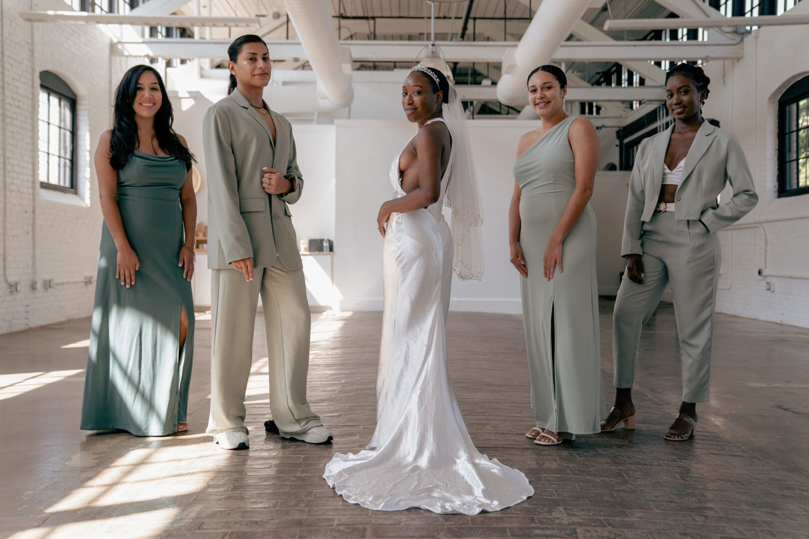 Bride posing with her bridesmaids in matching sage green dresses