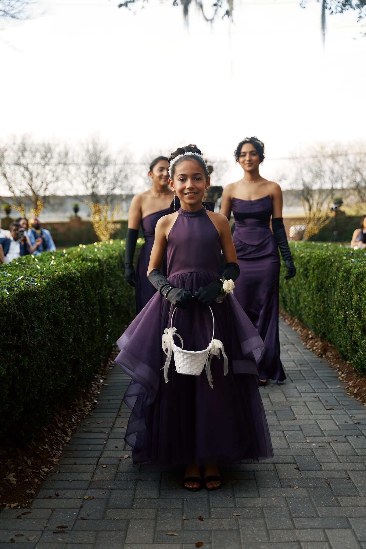 Flower girl in purple gown walking down the wedding aisle