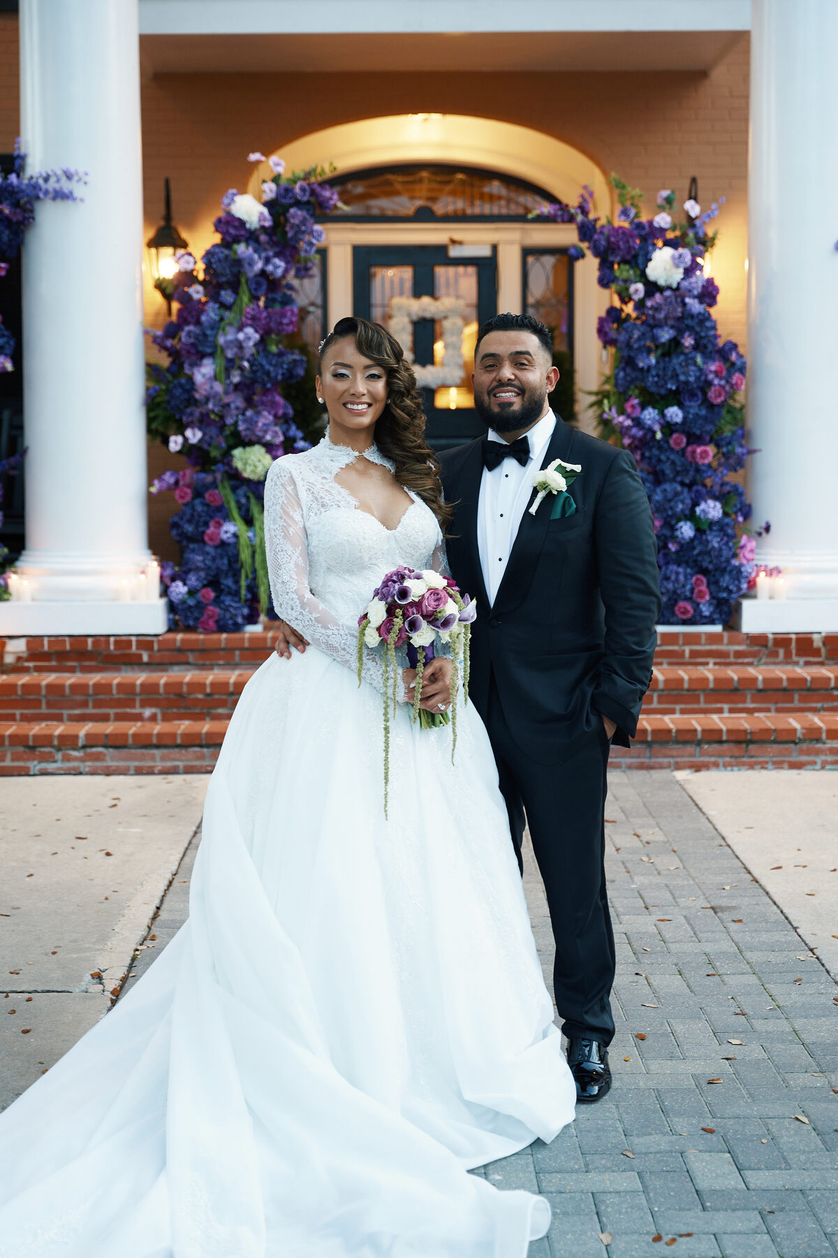 Bride and groom portrait framed by a purple floral entrance arch