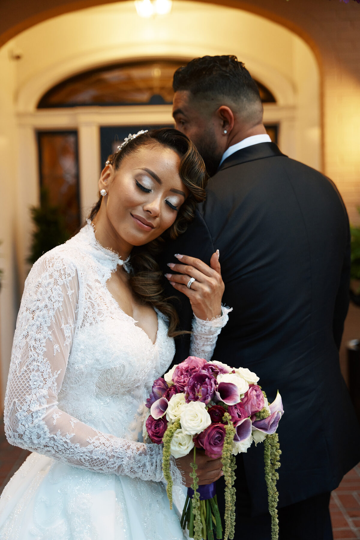 Groom kissing bride's hand beneath a floral archway entrance